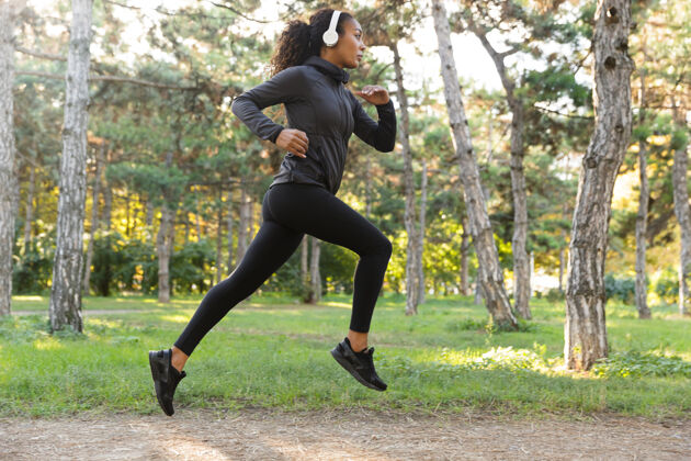 运动20多岁的女性穿着黑色运动服 戴着耳机 在绿色公园里跑步散步公园非洲