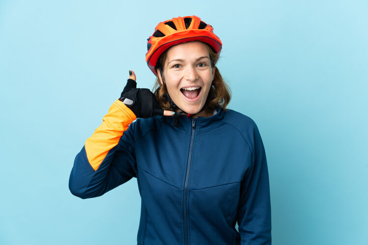 骑自行车一个骑自行车的年轻女子在蓝色背景下做着电话手势回我电话标志格鲁吉亚运动头发
