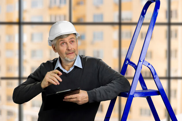 建筑工人成熟的工头往上看年长的工程师用剪贴板检查施工发展头盔工程师