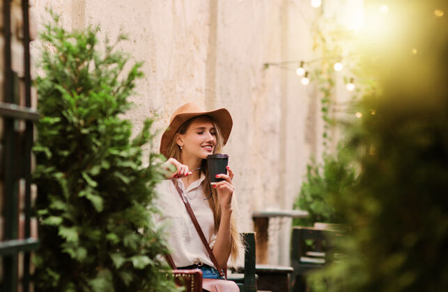 城市年轻的女游客在一个老式的户外咖啡馆里享受着一杯咖啡光泽帽子肖像