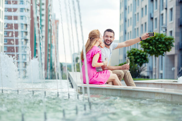 消遣漂亮的照片很好的积极的男人坐在一起和他的女朋友一起自拍喷泉休闲感情