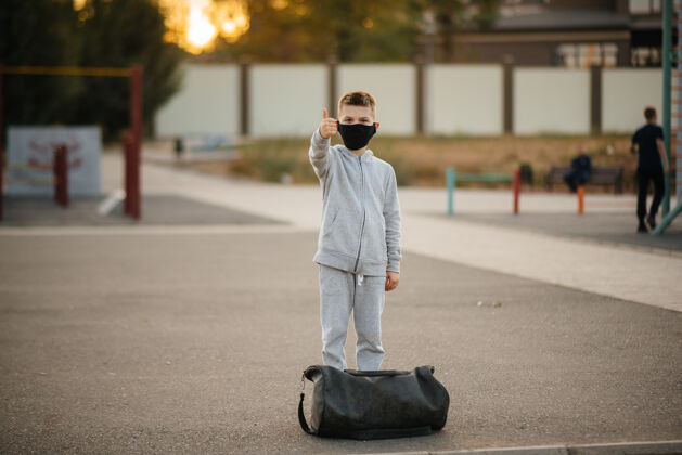 肖像日落时分 一个男孩戴着口罩站在运动场上进行户外运动流感大流行期间 他过着健康的生活方式健康的生活方式病毒防护流行病