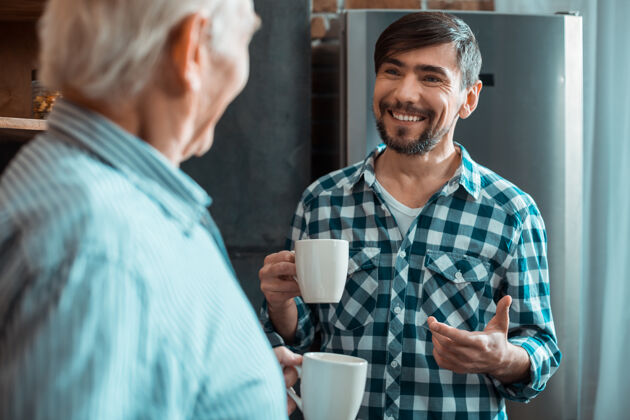 世代快乐的男人捧着一杯茶 微笑着向父亲诉说 同时享受着家庭的气氛房子医疗保健舒适