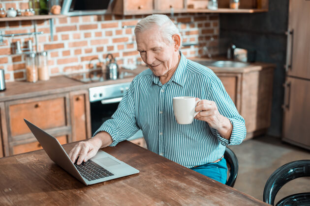 娱乐快乐的老人坐在笔记本电脑前 一边在家休息一边喝着饮料退休医疗保健互联网