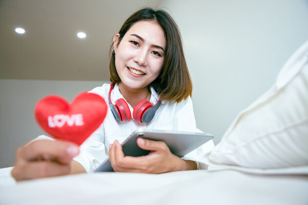放松亚洲美女在情人节用平板电脑买礼物 在卧室里展示爱心文字积极女人年轻
