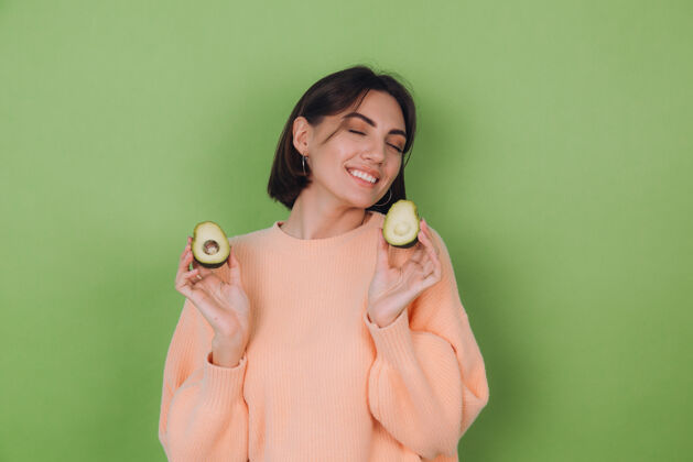 卡路里年轻女子穿着休闲桃毛衣隔离在绿橄榄墙上捧着鳄梨 健康护肤理念 复制空间蔬菜女人微笑