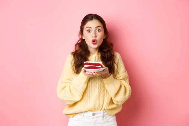 魅力庆祝和节日兴奋的生日女孩拿着蜡烛拿着生日蛋糕 站在粉红色的墙上惊讶地看着相机蛋糕休闲女孩