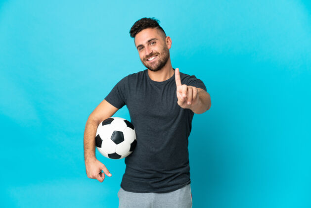 人一个足球运动员在蓝色的背景下展示并举起一个手指竞争成人分