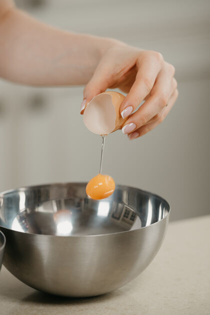 手工一个女人的手在厨房的不锈钢碗上滴蛋黄的亲密照片配料白厨师