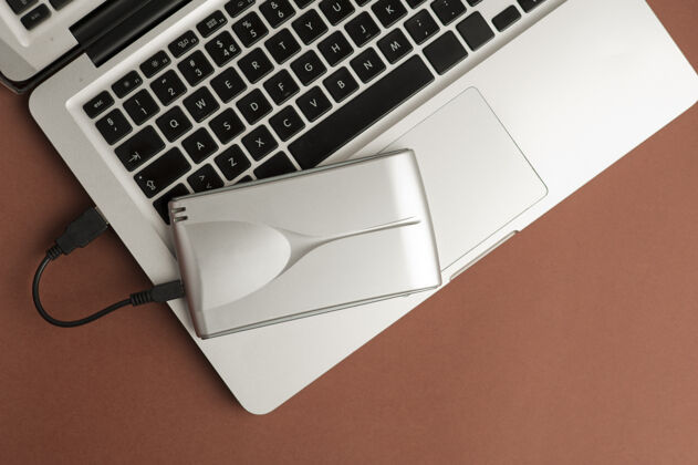 桌面特写铝外置硬盘在笔记本电脑上的棕色办公桌面视图笔记本电脑设备笔记本电脑