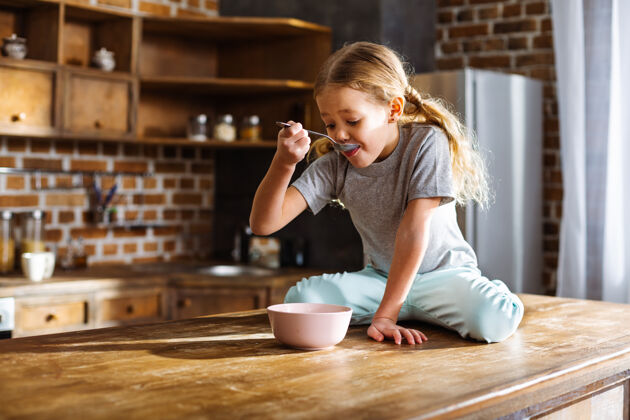 年轻可爱的小女孩坐在厨房里吃麦片小玻璃厨房