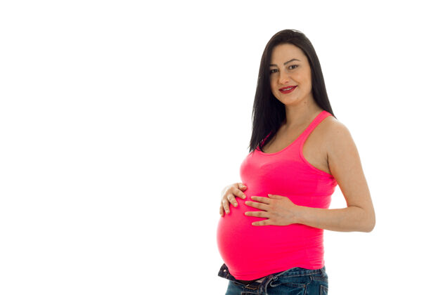 肚子穿着粉色衬衫的年轻黑发孕妇在白墙上摆出孤立的姿势房子快乐保健