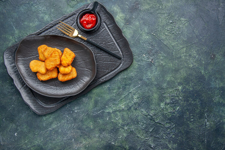 烹饪特写镜头的鸡块在一个黑色的盘子和叉番茄酱在右侧的深色托盘上正餐健康节食