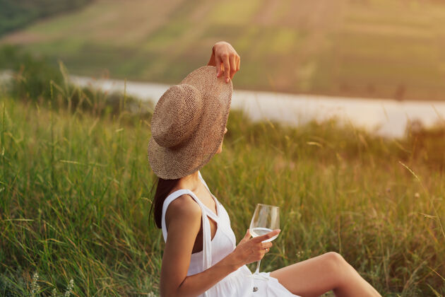葡萄酒一位身着白裙 头戴草帽 手拿酒杯的优雅女孩正在大自然野餐的特写镜头自然帽子女孩