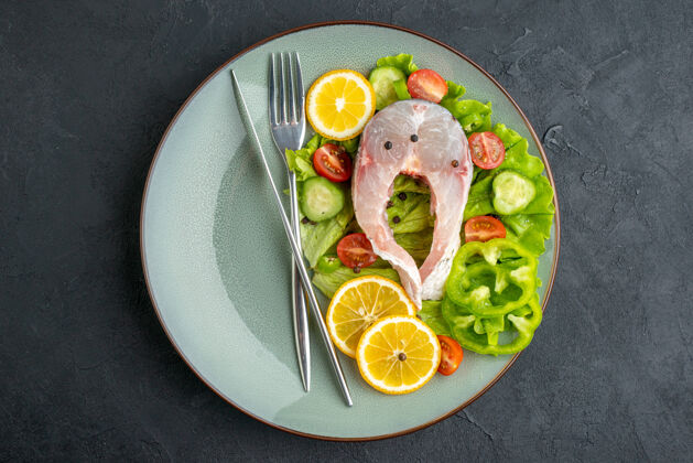 晚餐上图：生鱼片和新鲜蔬菜柠檬片和餐具放在黑色表面的灰色盘子上 有自由空间柠檬蔬菜餐具
