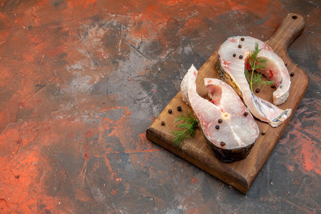鞋新鲜生鱼肉和胡椒粉的正面图 位于混合色表面左侧的木质砧板上 有自由空间混合物板胡椒