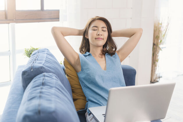 休闲亚洲女商人在家使用笔记本电脑工作舒展放松在沙发上呼吸新鲜空气社交距离概念教育观看设备