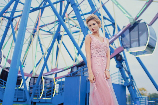女性穿着粉红色晚礼服的年轻漂亮女人在街上散步时尚公园摩天轮附近户外美丽女孩的风格肖像魅力华丽夜晚