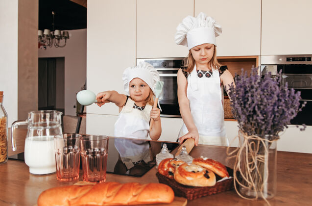 厨师两个戴着厨师帽和白围裙的可爱女孩在厨房里做饭面包师女孩面包