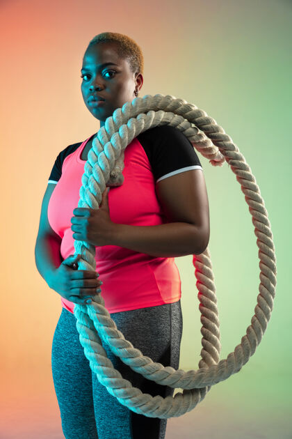 人年轻的非裔美籍大号女模特在霓虹灯下的梯度墙上训练力量体育肖像