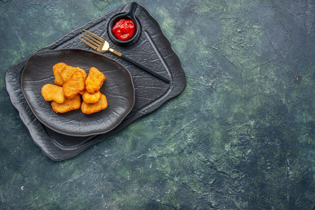 烹饪特写镜头的鸡块在一个黑色的盘子和叉番茄酱在右侧的深色托盘上正餐健康节食