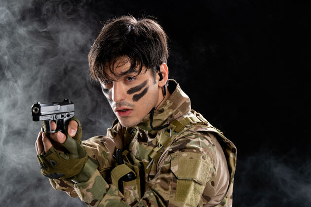 军装黑墙上穿着迷彩服持枪的年轻士兵的正视图视图肖像人