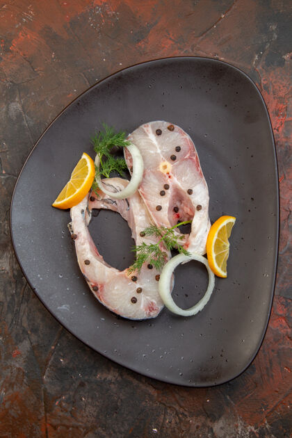 切片生鱼片和胡椒柠檬片的俯视图在混合色表面的黑色盘子上盘子胡椒晚餐