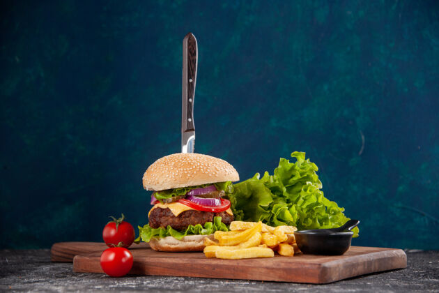 刀刀在肉三明治和薯条番茄干在木板番茄酱在深蓝色的表面蔬菜午餐饮食
