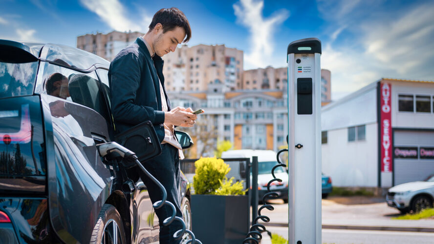 电力男人在充电站给他的电动车充电 用智能手机电动车电池电缆