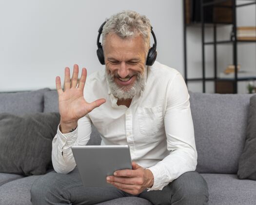 房子家里的老人坐在沙发上用平板电脑打视频电话 戴着耳机胡须家庭耳机