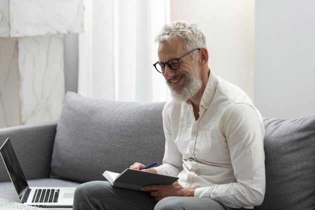 男人在家学习笔记本电脑和做笔记的老人老人室内沙发