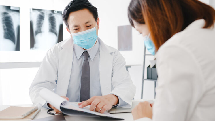 外科严肃的亚洲男医生戴着防护面具用剪贴板发表新闻谈话讨论结果社交距离诊所暴发