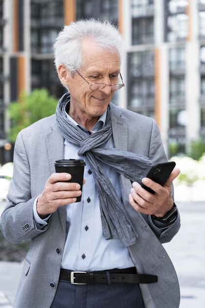 老年人城里时髦的老人一边喝咖啡一边用智能手机成熟户外男人