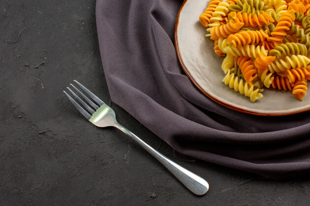 叉子顶视图煮熟的意大利面食不寻常的螺旋面食在深色桌子上的盘子里面食晚餐食物烹饪菜肴器具螺丝刀抹刀