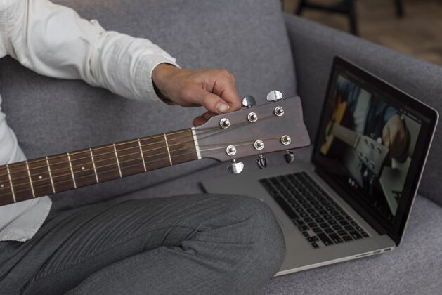 原声吉他老人在家的沙发上用笔记本电脑学习吉他课老年人成熟学习