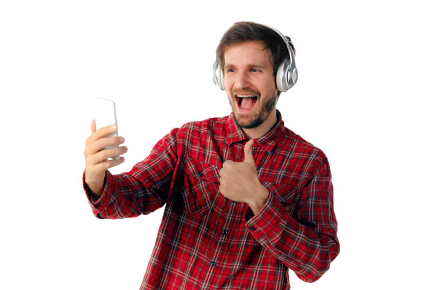 年轻拍摄年轻的白人男子使用移动智能手机 耳机上的白色工作室背景隔离现代技术的概念 小玩意 技术 情感屏幕互联网商务
