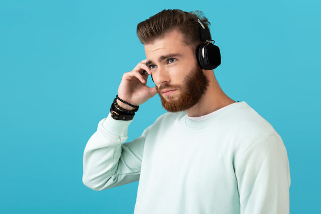表情时尚迷人的年轻留胡子的男人在无线耳机上听音乐的肖像现代风格自信的心情家伙时髦城市