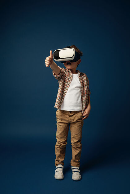 虚拟现实为其他星球带来和平穿着牛仔裤和衬衫 戴着虚拟现实耳机眼镜的小男孩或儿童 蓝色工作室背景尖端技术的概念 视频游戏 创新护目镜儿童眼镜
