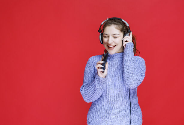 促销戴着耳机的女孩在她的智能手机上放音乐 享受着它女性休闲服装