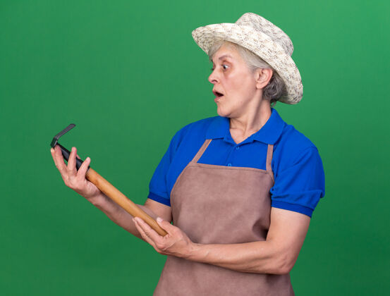 举行兴奋的上了年纪的女园丁戴着园艺帽拿着耙子看着兴奋老人女性