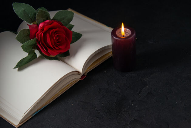 黑暗打开的书与蜡烛和红花在黑色的正面视图庆典玫瑰花