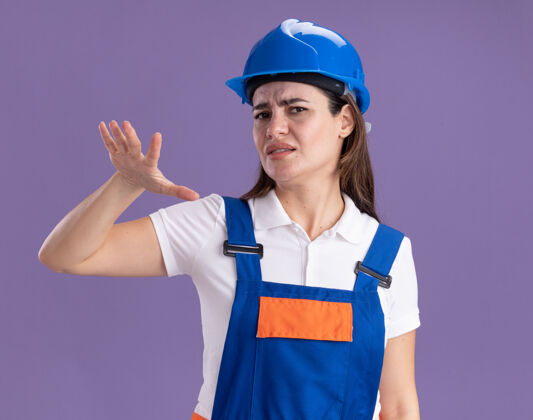 年轻人一个穿着制服的年轻建筑女工在紫色的墙上展示着孤立的尺寸表演衣服人