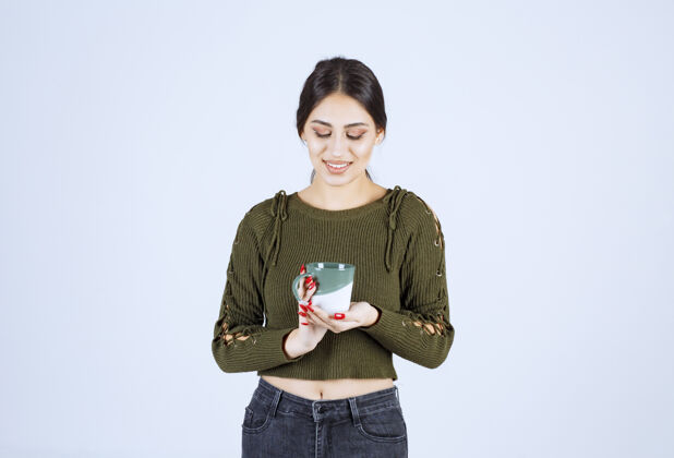 摆姿势一个穿着绿色毛衣的年轻漂亮的女模特在看一个杯子站着杯子水
