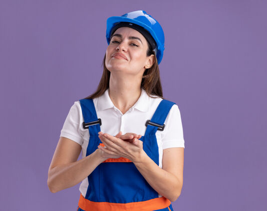 手自信的穿着制服的年轻建筑女手牵手孤立在紫色的墙上自信握着建设者