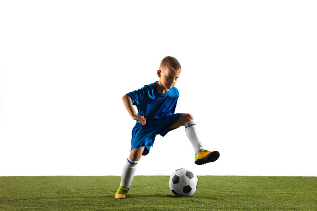青少年穿着运动服的足球或足球运动员的小男孩在白色工作室背景上用球假装或踢进球适合在比赛中扮演男孩的动作 动作 动作草地比赛孩子