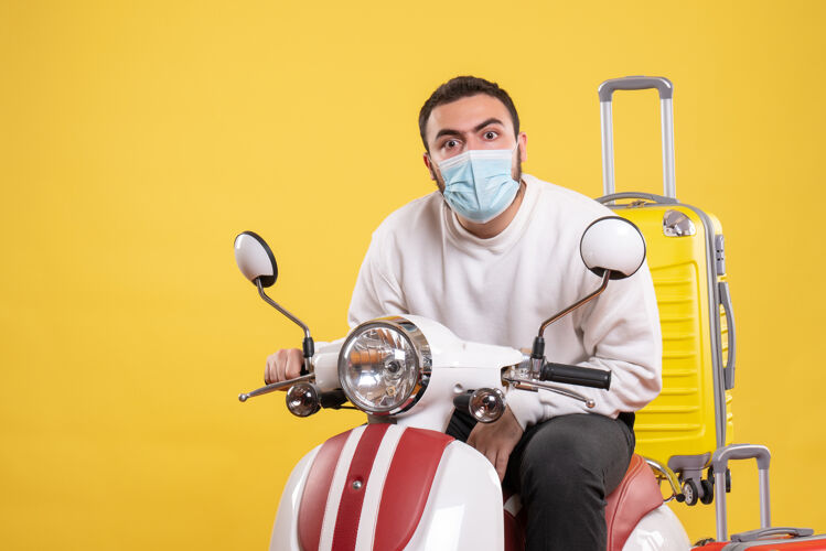 手提箱旅行概念与惊讶的家伙在医疗面具坐在摩托车上 黄色手提箱上黄色运动比赛剑
