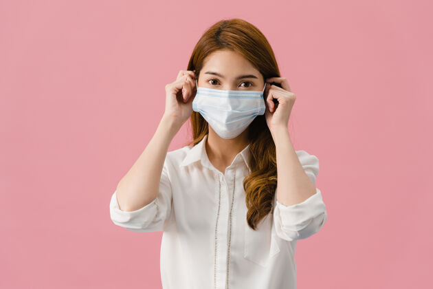 严重年轻的亚洲女孩戴着医用面罩 穿着休闲服 看着隔离在粉色背景下的相机医学担心肖像
