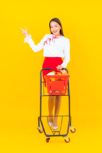 杂货店一幅美丽的亚洲年轻女子的画像 黄色的是超市里的购物篮女性购买购物车