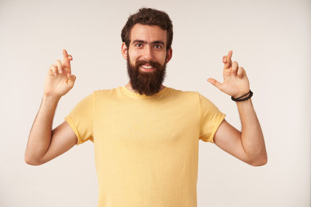 自信留着胡子的年轻人的肖像 穿着黄色t恤休闲风格 交叉着手指站着墙姿势男人