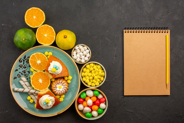 盘子俯瞰美味的派片 配上糖果和新鲜的橘子 背景是深色的水果蛋糕 甜甜的饼干派顶部蛋糕橘子